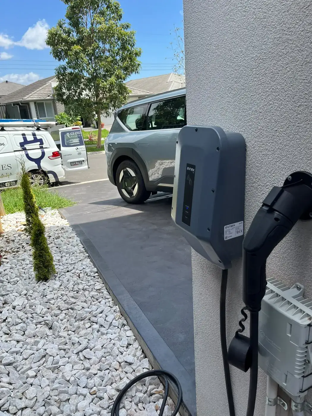 An EV charger installed on a house wall beside the driveway, with the car parked alongside