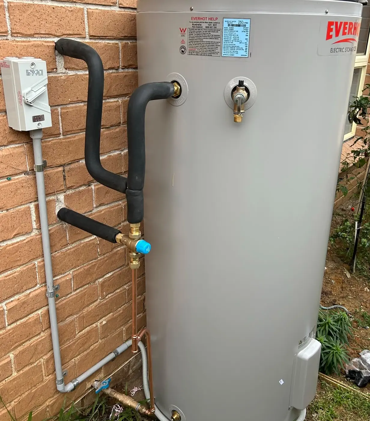 An electric storage hot water system installed by C3 Industries, with its weatherproof isolator switch and conduit run down the brick wall