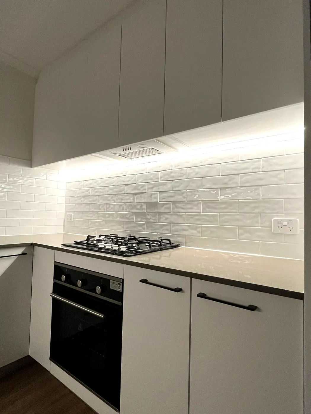 A wall oven and gas cooktop installed by C3 Industries beneath a lit LED strip and a rangehood