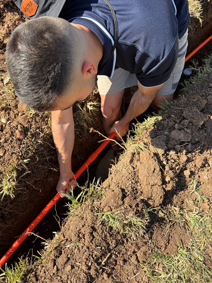 C3 Industries laying orange electrical conduit in a trench to run underground power to an outbuilding